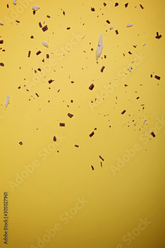 White and dark chocolate pieces and chipson on a bright yellow background. View from above. Flat lay.