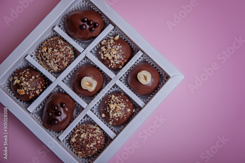 Chocolate candies in paper tartlets in a box on a pink background. View from above. Flat lay.