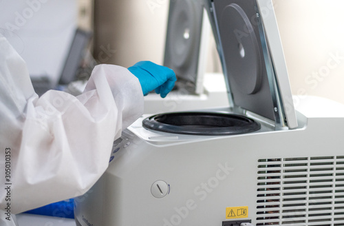 Laboratory technician using centrifuge device automation machine for testing and diagnostic clinical specimens sample in lab room of hospital. Medical science technology concept.
