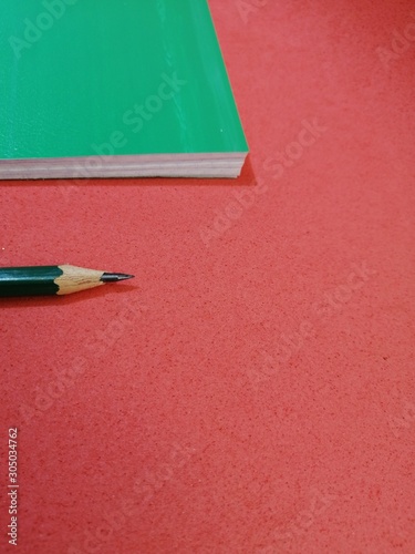cooked closed green notebook with black pencil on a red background