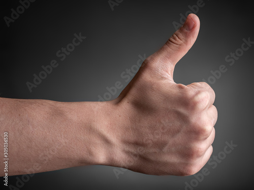 Male hand on a gray background shows thumb up.