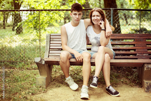 A teenage boy with his mother sitting on a bench in the park in the summer and talking. They are trying together to overcome the problems of adolescence