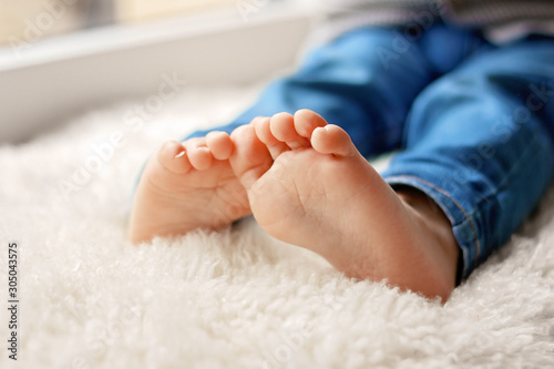 Cozy holidays at home. Close up photo of little child barefooted feet sitting on white furry blanket at window. Winter season lifestyle. Leisure time. Sweet childhood. Copy space