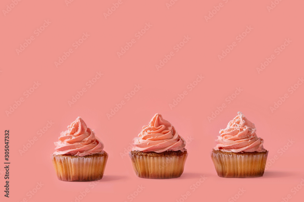 Three homemade cupcakes with pink buttercream and coconut flakes in row over red pink background. Three homemade cupcakes with pink buttercream and coconut flakes in row over red pink background.