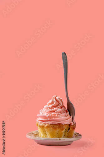 Homemade cupcake with pink buttercream and coconut flakes, with dessert fork within over red pink background.