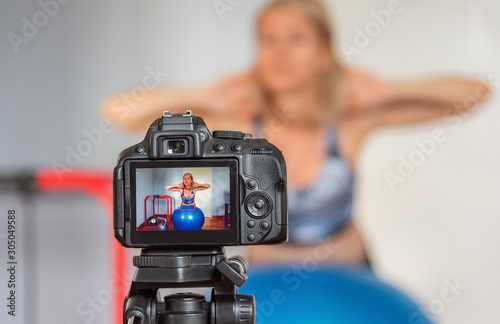 DSLR camera in front of fitness blogger recording a video blog about sports and home workout.