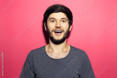 Portrait of young surprised man isolated on coral pink background.