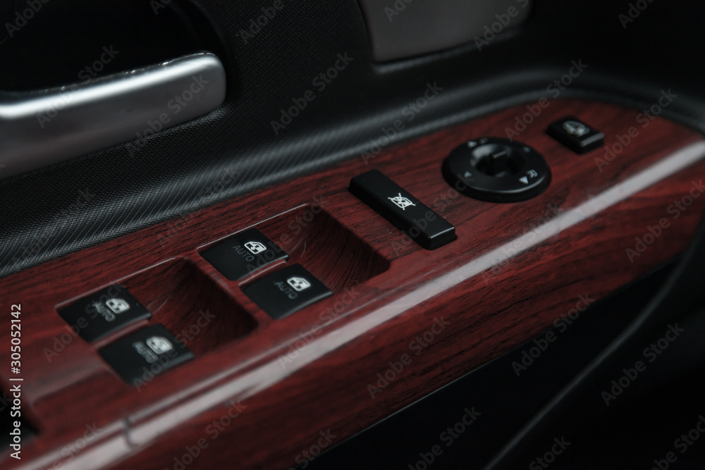 The control buttons for opening and closing windows of doors and electric controls and settings of mirrors on the door in black with leather upholstery in a luxury modern car.