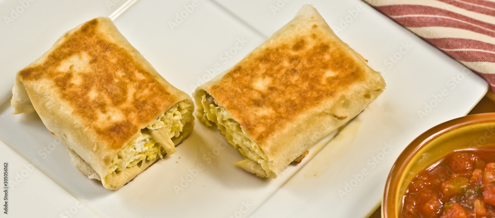 Top view, close up of a halved crab burrito on a square, white plate and bowl of chutney Top view, close up of a halved crab burrito on a square, white plate and bowl of chutney