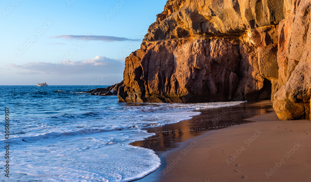 Beautiful Gran Canaria beach at sunset. Rocky shore, grotto and footprints in the sand.
