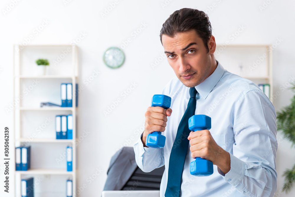 Young handsome employee doing sport exercises at workplace Young handsome employee doing sport exercises at workplace