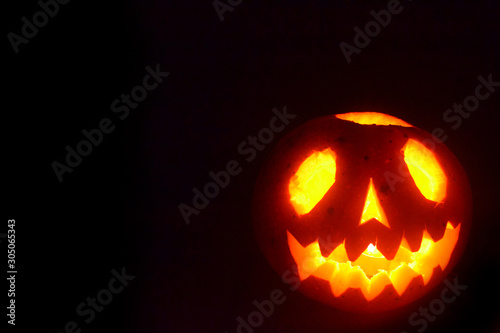 Black Halloween background with a glowing jack-o-lantern. Photo of scary pumpkin.
