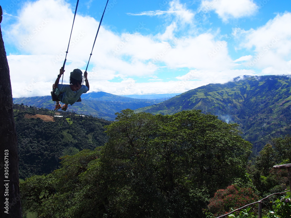 Obraz premium A young man sitting on a large wooden swing at the treehouse under a beautiful sky, La casa del Arbol (La Casa del Árbol), Banos (Baños), Ecuador