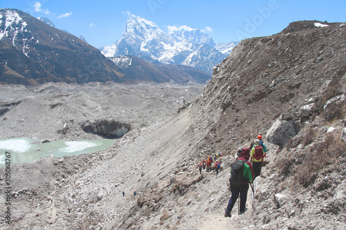 A group of hikers descends on a Ngozumpa glacier in Himalayas. Lake of melted ice is visible in the middle of glacier. Route to Everest base camp through Gokyo lakes.