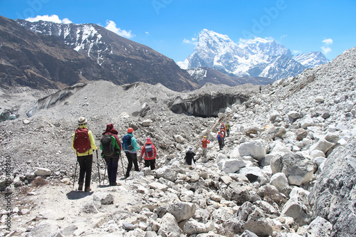 A group of hikers walks through a Ngozumpa glacier in Himalayas. Cholatse and Taboche mountain peaks are visible in the background. Route to Everest base camp through Gokyo lakes. photo