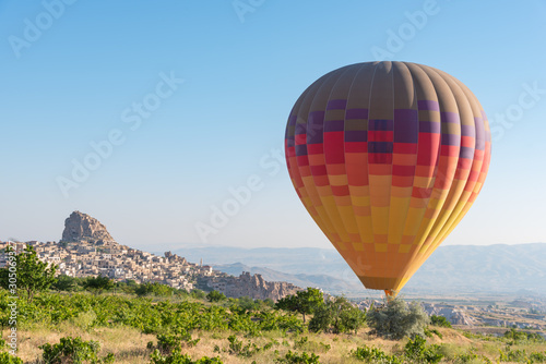 One hot air balloon flying low over the field. Uchisar castle on background, Cappdocia, Turkey. © 22Imagesstudio