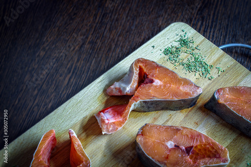 Four pieces of pink salmon lie on a cutting Board made of wood with herbs and spices