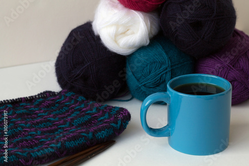 blue cup of black coffee with colour balls of wool yarn and knitting on white background