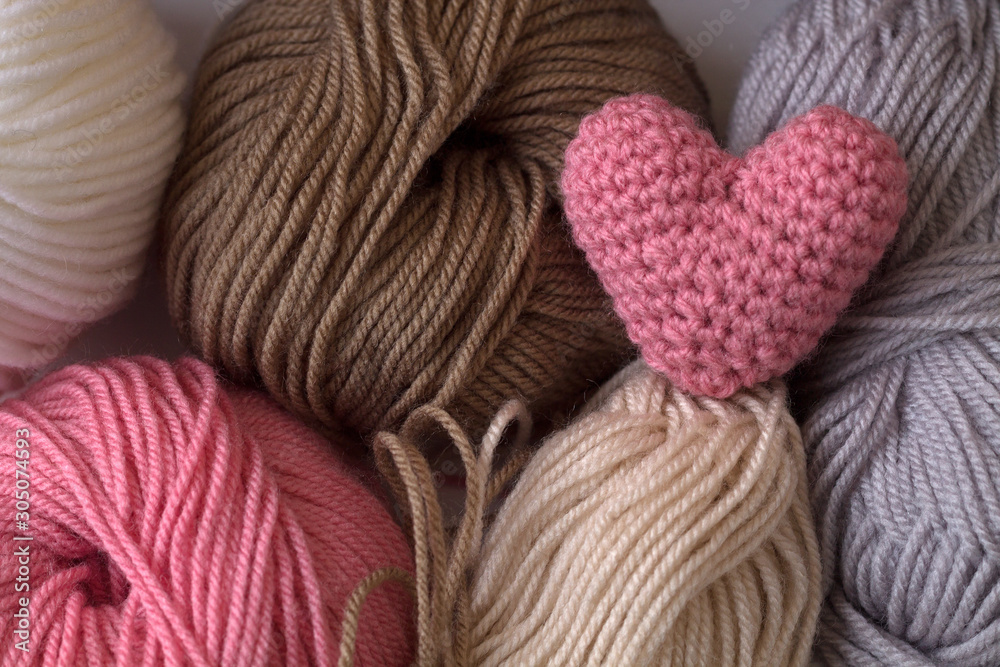 Pink knitted heart of yarn on colored skeins of yarn. top view Pink knitted heart of yarn on colored skeins of yarn. top view
