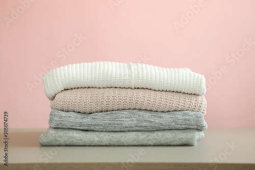 a stack of warm sweaters on the table on a colored background.