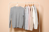 Warm sweaters on a wardrobe hanger on a colored background. Autumn, winter clothes.
