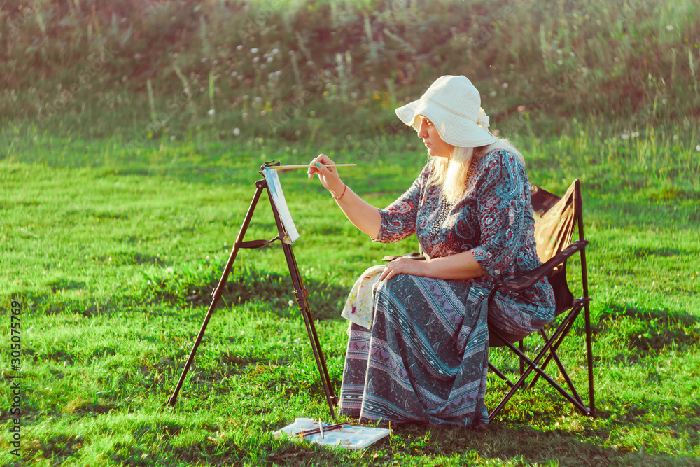 an elderly woman paints a picture in nature an elderly woman paints a picture in nature