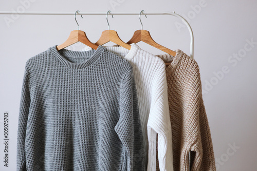 Warm sweaters on a wardrobe hanger on a light background. Autumn, winter clothes. photo