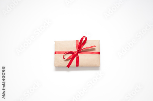 Fototapeta Naklejka Na Ścianę i Meble -  Gift isolated on a white background, Packed in brown paper and decorated with a red ribbon with a bow, there is a place for the inscription. The concept of surprises and gifts.