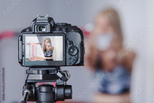 Young caucasian woman recording herself during sports dietary video blog on DSLR camera. Unfocused woamn, focused camera screen.