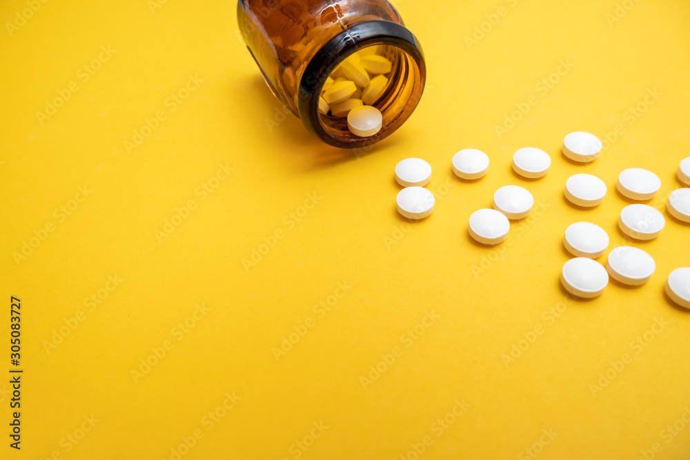 Many white tablets and brown glass container close up on yellow background with copy space, autumn and winter viral disease , infection Many white tablets and brown glass container close up on yellow background with copy space, autumn and winter viral disease , infection