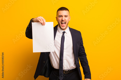 young handsome businessman  against flat background holding an empty piece of paper