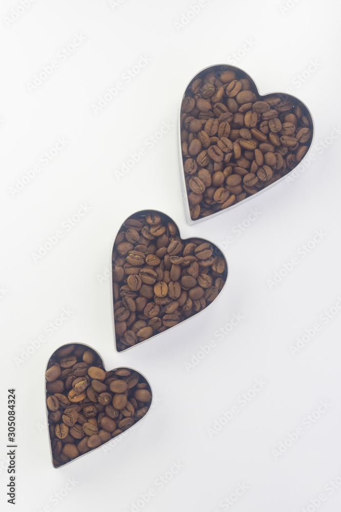 Obraz premium coffee beans in three tins of different sizes in the shape of a heart arranged diagonally one after another on a white background Flat lay