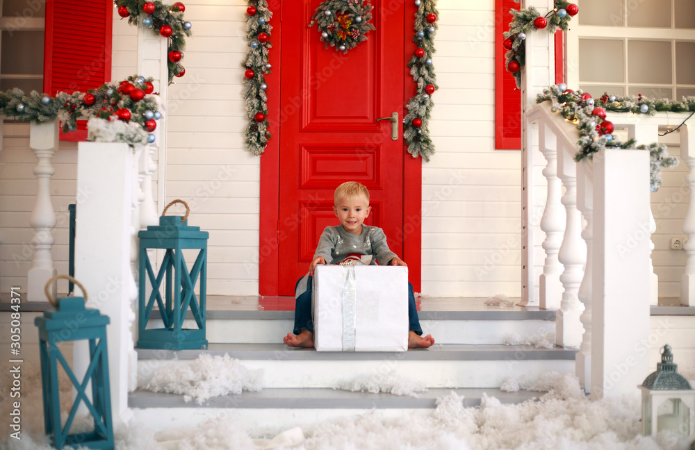 Little boy child with gift in yard at home in Christmas decorations Little boy child with gift in yard at home in Christmas decorations