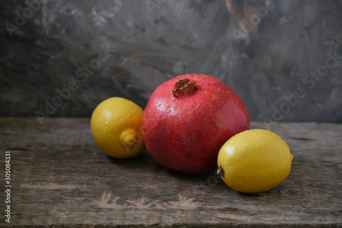 Fruits, pomegranates and two fresh lemons lie on a wooden table.