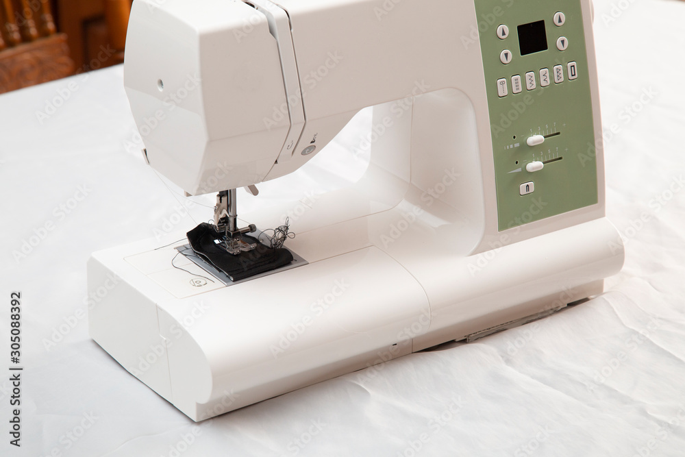 Modern sewing machine is used at home for sewing clothes.
