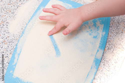 a small child draws a finger with semolina, a kitchen table, the development of fine motor skills, what to do with a child, cutting board blue