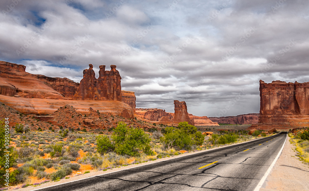 The road passing through the Arches National Park against the backdrop of a stormy sky and mountain landscape.
