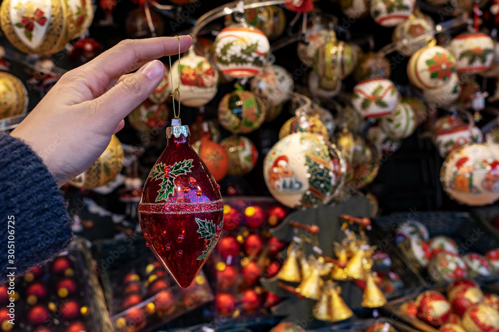 woman holding hanging Christmas ornament decoration with kiosk stand on a winter market background
