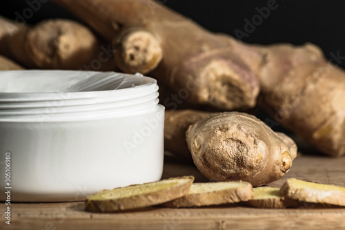 Cosmetics body cream container with ginger oil extract on wooden table. ginger roots and slices. 