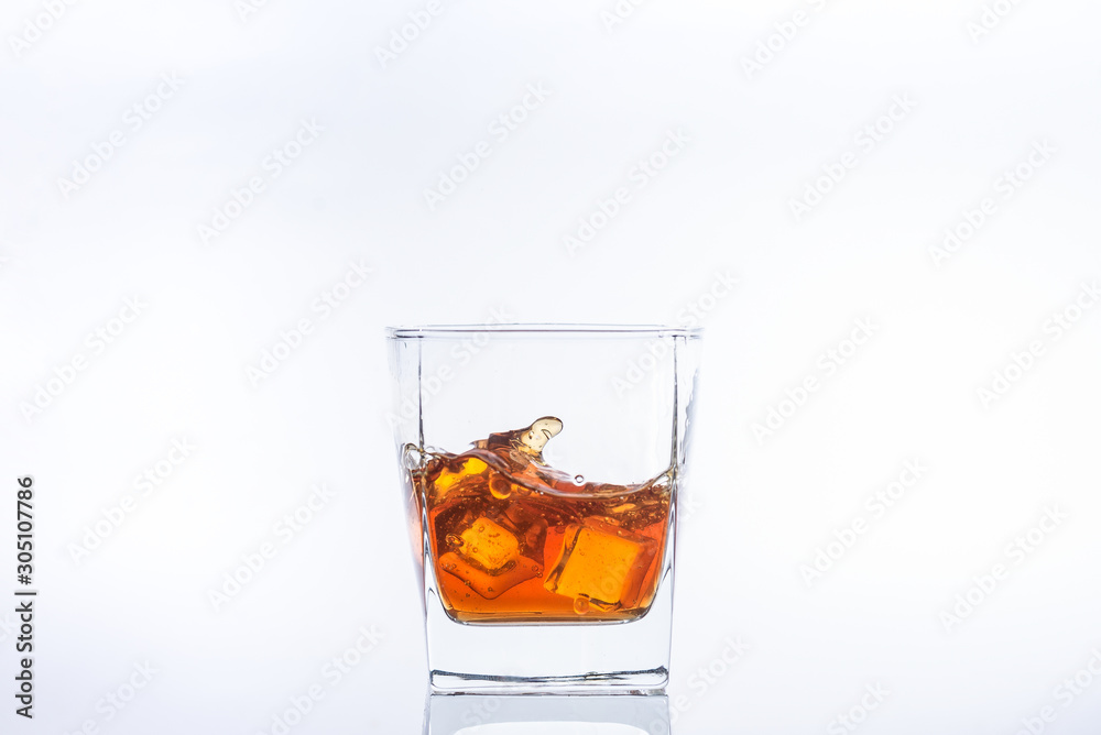Two ice cubes in a glass of whiskey with splashes. Ice cubes in a glass with alcohol