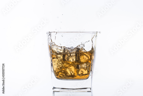 Whiskey with ice. Rum with ice. Brown brandy with ice. Three ice cubes in a glass with alcohol. Сubes fall into a glass with splashes.