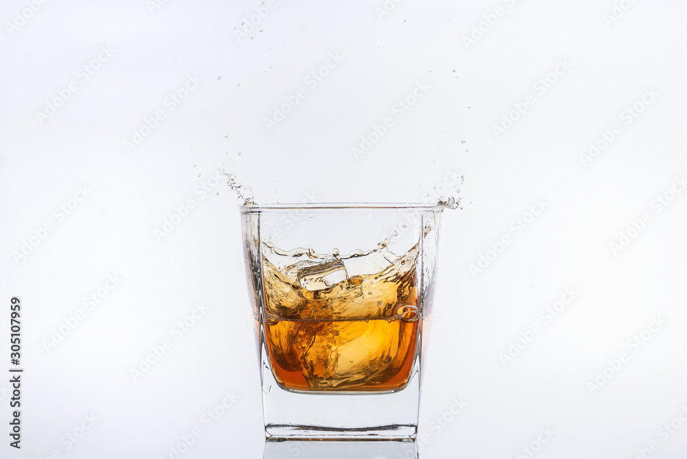 Alcohol drinks. Whiskey with ice. Rum with ice. Brown brandy with ice. Ice cube falling with splashes into a glass with alcohol Alcohol drinks. Whiskey with ice. Rum with ice. Brown brandy with ice. Ice cube falling with splashes into a glass with alcohol