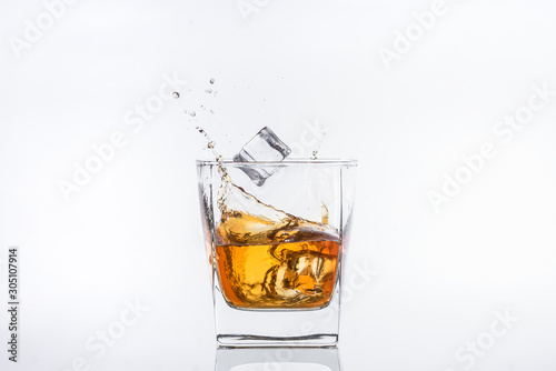 Whiskey with ice. Rum with ice. Brown brandy with ice. Ice cube falls into a glass with splashes.