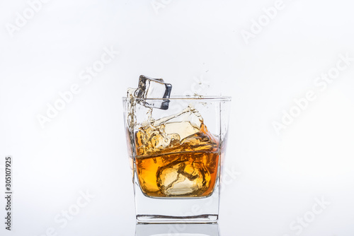 Whiskey with ice. Rum with ice. Brown brandy with ice. Two ice cubes falling with splashes into a glass with alcohol