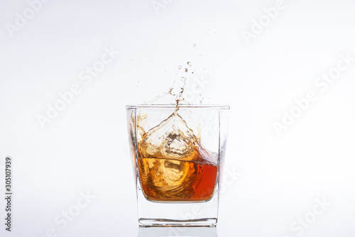 Whiskey and ice. Rum with ice. Brown brandy with splashes. Ice cube falls into a glass with splashes