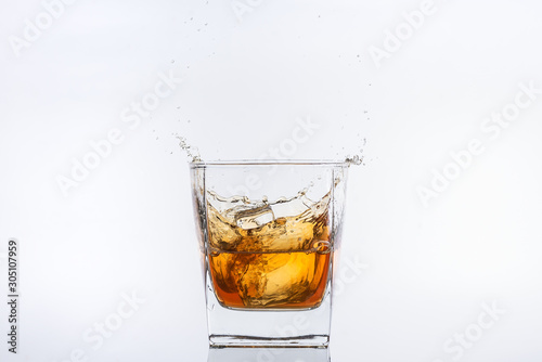 Alcohol drinks. Whiskey with ice. Rum with ice. Brown brandy with ice. Ice cube falling with splashes into a glass with alcohol
