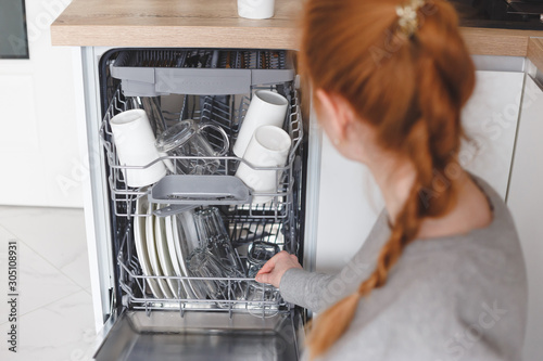 Housework: young woman putting dishes in the dishwasher