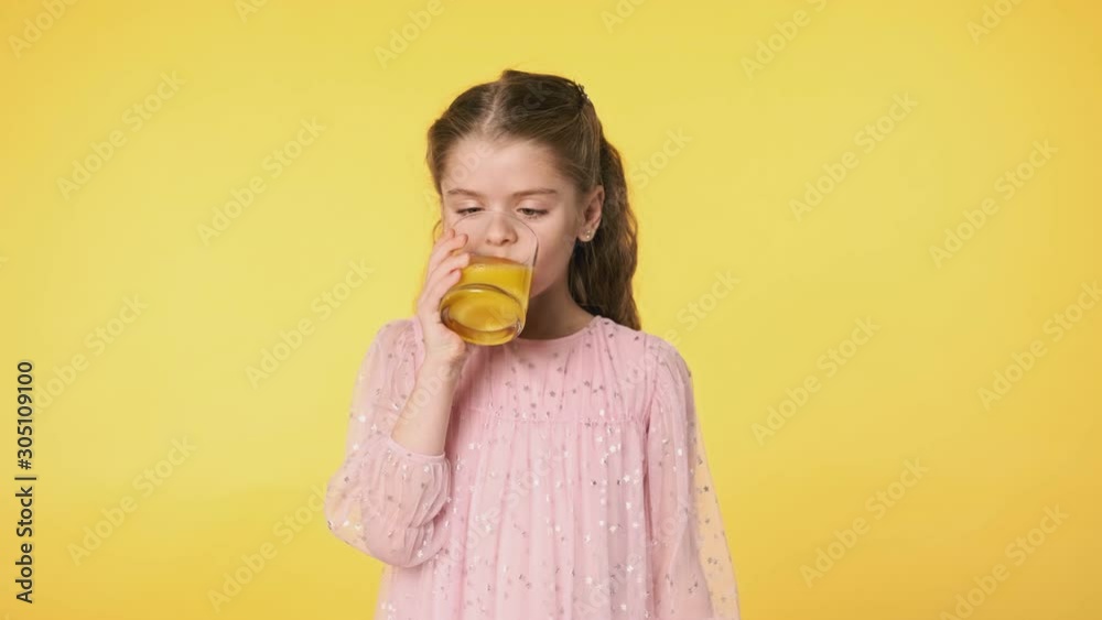 Medium portrait of child with glass of juice. Beautiful kid girl drinking orange juice from glass at yellow background. Slow motion. 4K, UHD Medium portrait of child with glass of juice. Beautiful kid girl drinking orange juice from glass at yellow background. Slow motion. 4K, UHD
