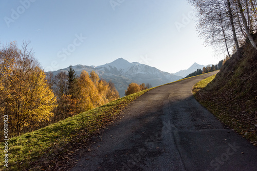 Street and hiking trail in autumn up the Keilberg, Schmittenhöhe in Schüttdorf, with peak of Kitzsteinhorn in background, Zell am See, Salzburger Land, Austria.