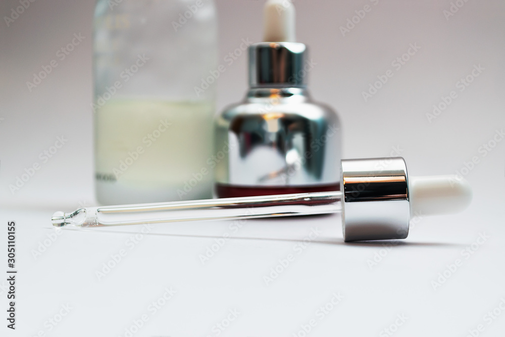 Close up on glass skincare pipette and unfocused cosmetics bottles on background. Skincare products concept. Close up on glass skincare pipette and unfocused cosmetics bottles on background. Skincare products concept.